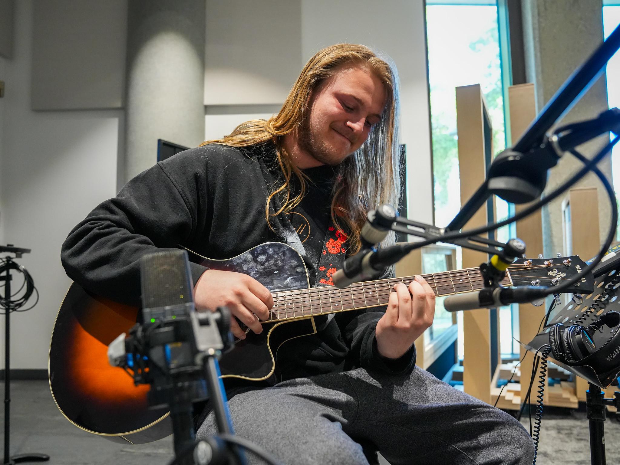 male student with long blonde hair playing a sunburst acoustic guitar