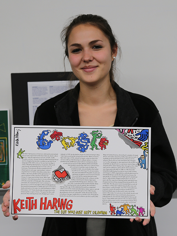 female student with brown hair in ponytail holding her keith karing poster