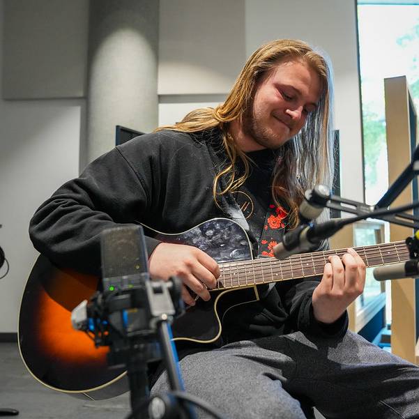 blonde guitarist playing barre chord on a sunburst acoustic guitar