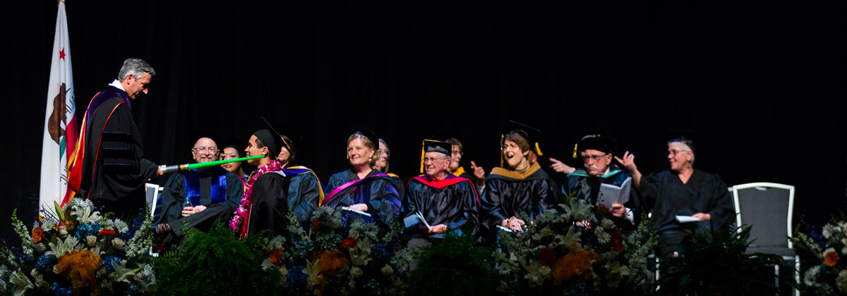 President Brad Davis dubbing student with light saber on graduation stage