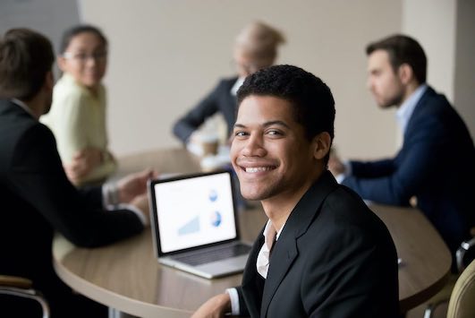 man professionally dressed seated at a table smiling at camera 