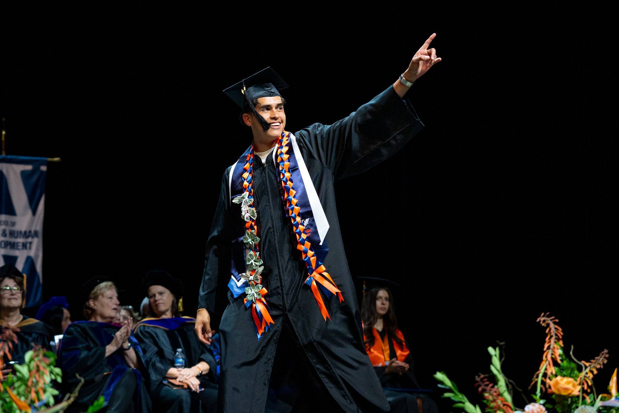 male commencement student in cap and gown pointing upwards