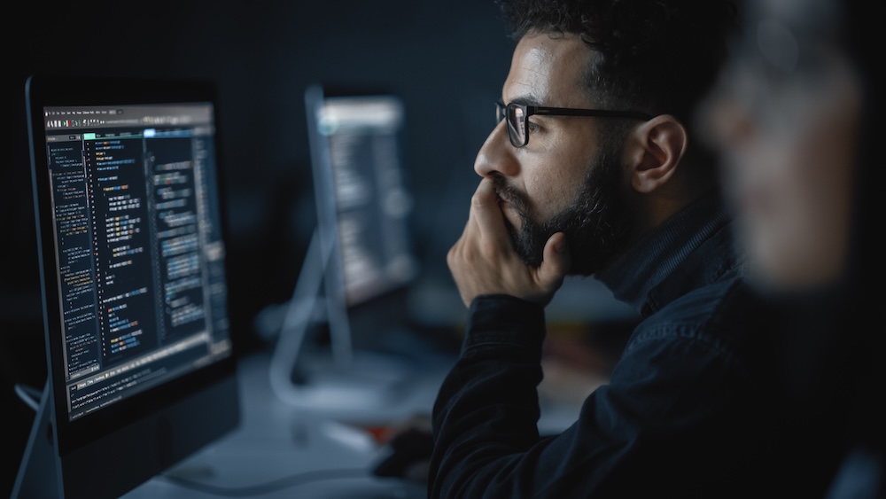 student on computer looking at monitor with code