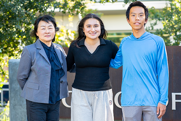 Two students with instructor smiling at camera outside of the science and math sign.