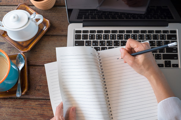 Laptop on desk with hands and notebook