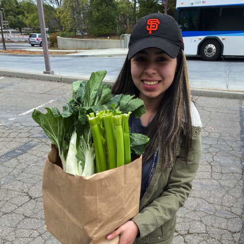 Student holding bag of groceries with celery exposed